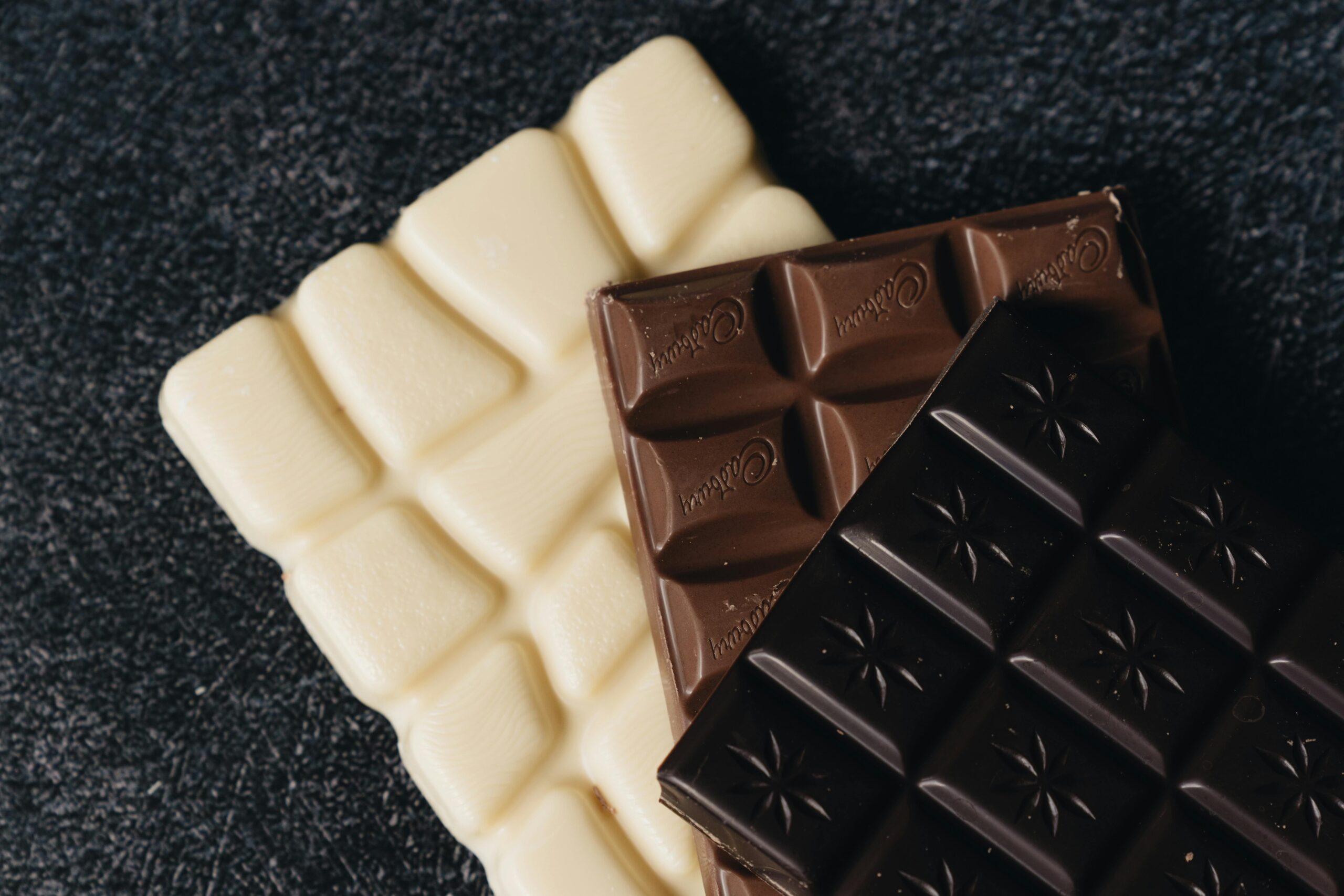 Close-up of assorted white, milk, and dark chocolate bars on a textured surface.